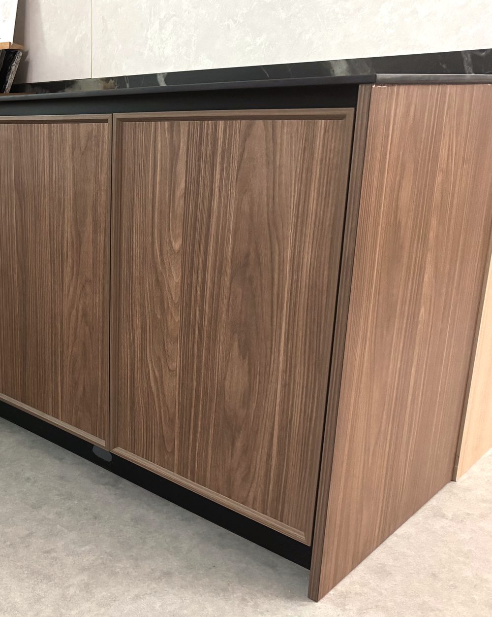 Walnut-tone kitchen cabinetry run with a black stone worktop at the CASAWAVE Woodlands showroom