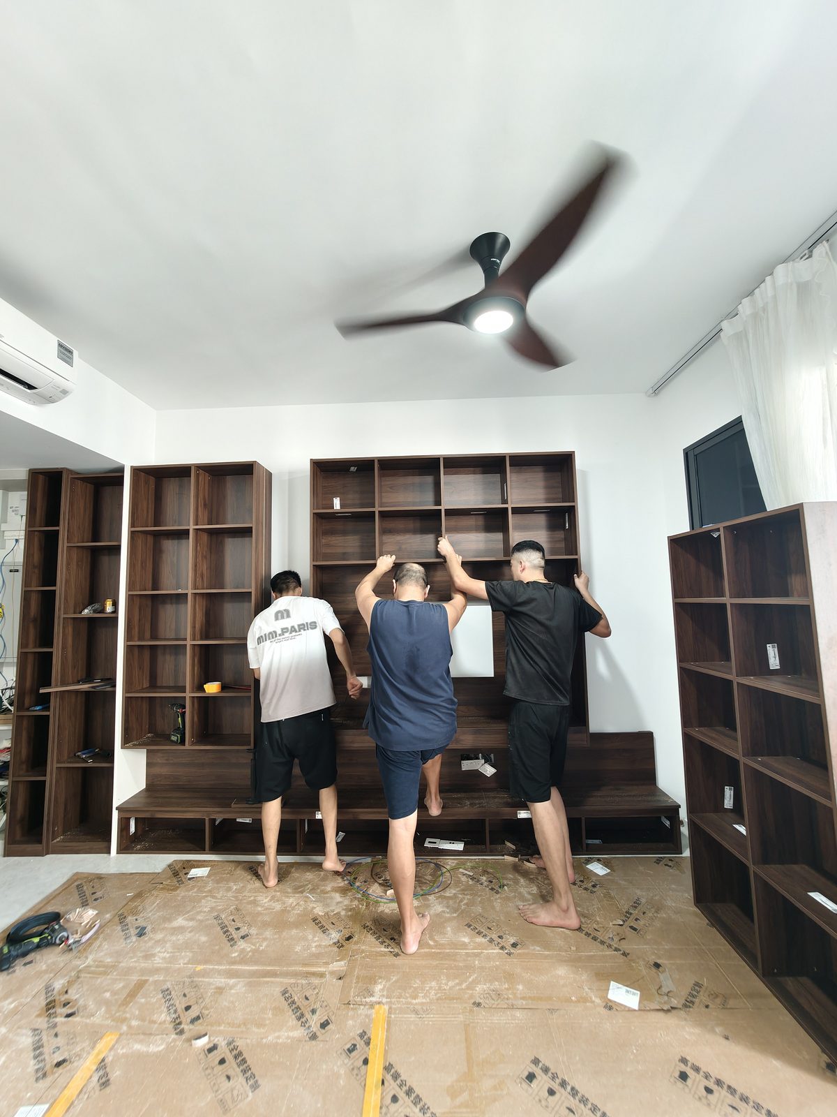 CASAWAVE team installing a full custom feature wall storage unit on a protected floor in a Singapore flat